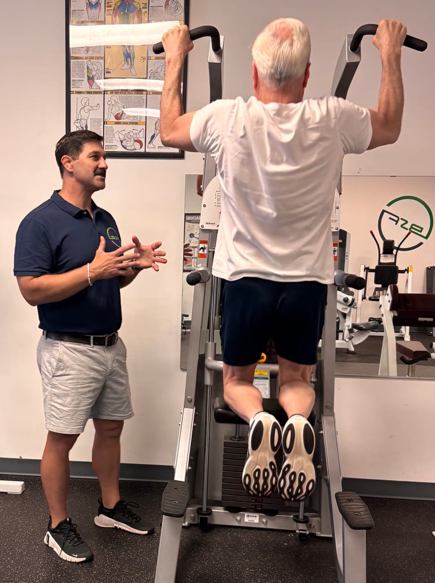 A personal training client performing a pull-up with Scott coaching